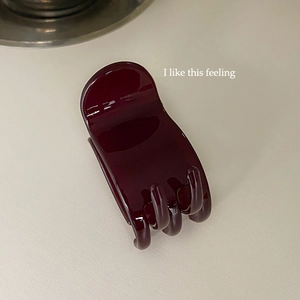 Detail view of burgundy wine red high gloss hair claw clip on beige surface