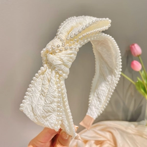 Detail of creamy white headband with large bow and hand-stitched faux pearls