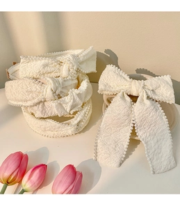 Macro detail of creamy white bow hairband with hand-stitched pearls and textured fabric
