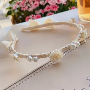 Detail eines cremefarbenen Satin-Haarreifs mit weißen Rosen, Perlen und Schleifen