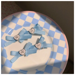 Détail de pinces à cheveux à nœud bleu clair avec breloques cœur sur assiette à carreaux