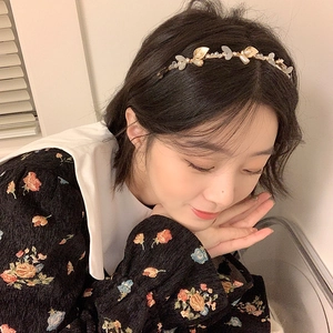 Elegant gold headband with white leaves and crystal beads worn by a model in soft light
