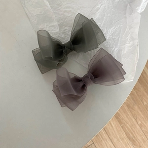 Detailed close-up of sage green and grey organza layered bow hair clips on paper