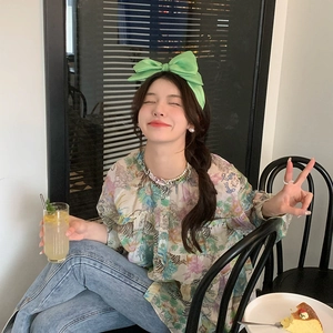 Chic female model wearing a large green velvet bow headband in a stylish cafe setting