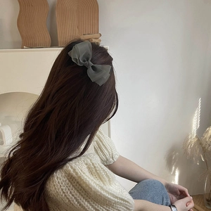Sage green organza bow hair clip shown on back of wavy hair in a French style