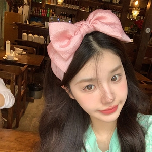 Close-up of a pink oversized satin bow headband worn by a woman for an elegant style