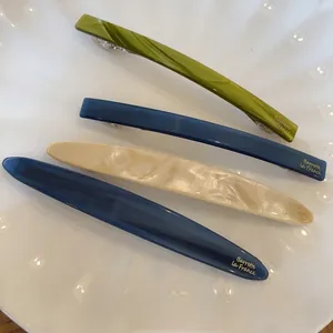 Detailed view of glossy acetate hair clips in green, blue, and cream with gold lettering