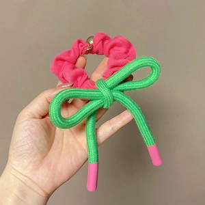 Détail du chouchou rose avec nœud tissé vert et perle dorée sur une main de femme