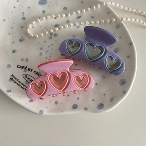 Pinzas para el pelo de acetato rosa y lila con corazones calados en un plato