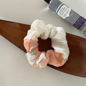 Detail eines geblümten Haargummis aus Chiffon auf einem Holztablett mit Blumenmuster