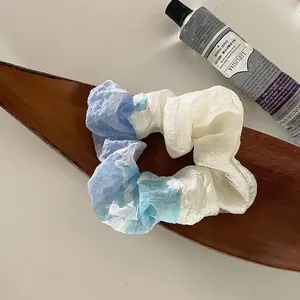 Detail eines blau-weißen Verlaufs-Haargummis aus Organza auf einem Holztablett für Styling
