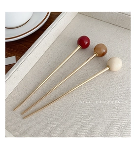 Close-up of three minimalist golden hairpins with colorful glass beads on a woven tray