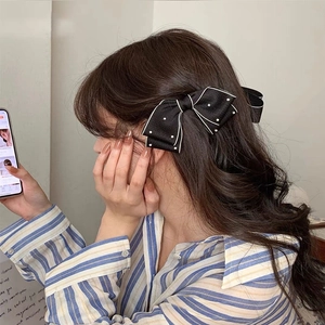 Detail of black fabric bow hair clip with white pearl dots worn by a female model