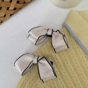 Detail of cream bow hair clips with white pearls and black edging on knit fabric
