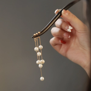 Detailed view of ebony wood hair stick featuring delicate pearl tassels and gold accents