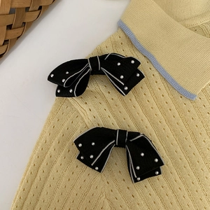 Close-up of black polka dot bow hair clips with pearls on yellow knit sweater fabric