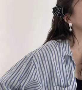Close-up of a black pleated bow hairpin and silver ball earring worn by a model