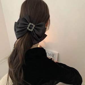Detail of a large black satin bow hair clip with a rectangular rhinestone center piece