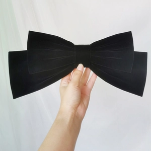 Detailed close-up of a large black velvet bow hair clip held by hand to show its scale