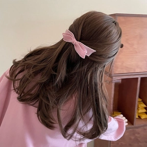 Pink fabric bow hair clip shown on model's wavy brown hair in a minimalist setting
