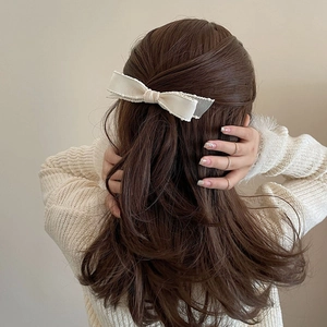 Detail of cream bow hair clip with wavy edges styled on wavy brown hair
