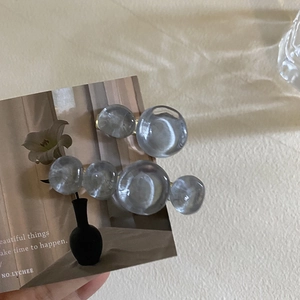 Close-up of translucent grey-blue resin beads on golden metal hair clips over a card