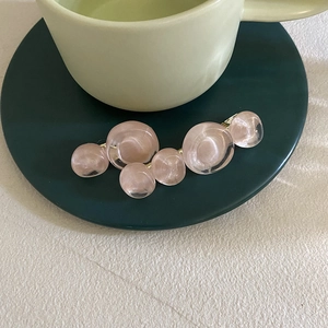 Detail of pink resin beads on a gold metal hair clip resting on a green ceramic tray