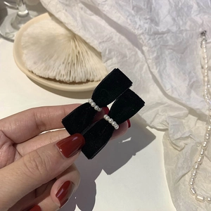 Detail view of vintage black velvet bow hair clips with elegant pearl accents in hand