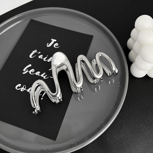 Minimalist silver wavy liquid metal hair claw clip displayed on a modern tray