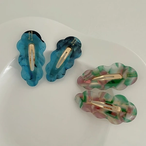 Detail of four cloud-shaped acetate hair clips with colorful marble texture and gold lettering