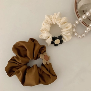 Detail of silk satin scrunchies in cream and bronze with flower charms on a desk