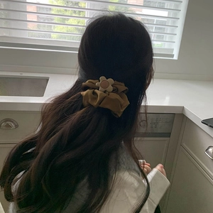 Brown silk scrunchie with cream flower charm worn on hair in a stylish ponytail