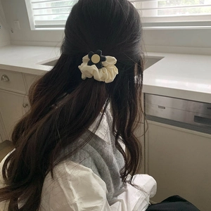 Detail of white ruffled scrunchie with black flower on brunette wavy hair in home setting