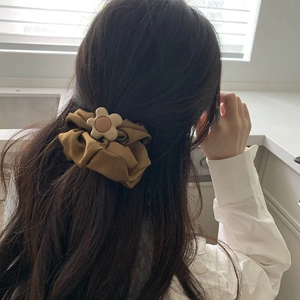 Detail of flower scrunchie in bronze silk-like fabric worn on model's wavy hair