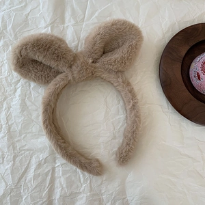 Close-up of soft plush rabbit ear headband in khaki on textured white background