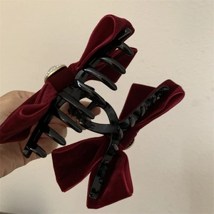 Détail d'une pince à cheveux en velours rouge avec nœud et perle décorative centrale