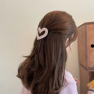 Detail of matte pink hollow heart hair clip with embossed logo on wavy brown hair