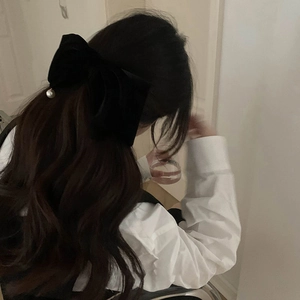 Dettaglio di un grande fiocco per capelli in velluto nero con perla bianca indossato dal modello