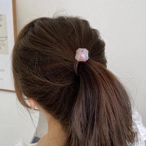 Gros plan d'un élastique à cheveux avec perle rose irisée sur une queue de cheval