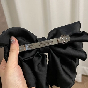 Détail du clip métallique argenté et du tissu en satin de la pince à cheveux nœud noir