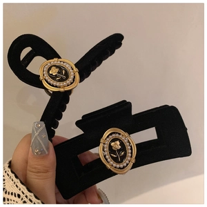 Close-up of black velvet hair clips with golden rose and pearl details in hand