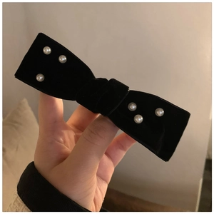 Detail of a black velvet bow hair clip with symmetrical white pearls in a vintage style