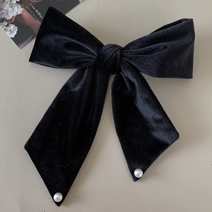 Elegant large black velvet bow hair clip with white pearl accents on minimalist background