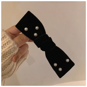 Close-up of black velvet bow hair clip with white pearls held against white knitwear