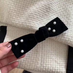 Elegant black velvet bow hair clip with pearls on tweed fabric background