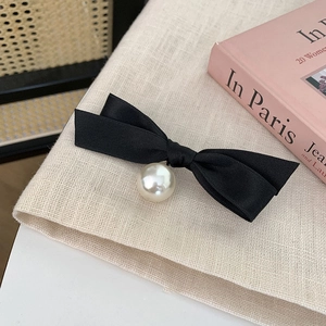 Detail of elegant black satin bow hair clip with a large white pearl drop pendant