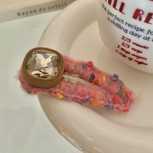 Detailed view of pink knitted hair clip with rhinestone and silver metal duckbill base