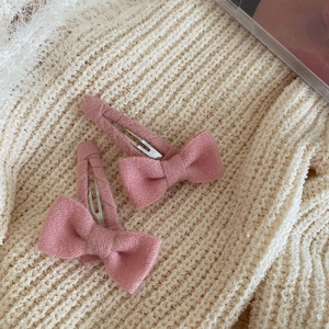 Gros plan de deux barrettes à nœuds roses avec texture mate sur fond tricoté