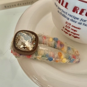 Detailed view of champagne rhinestone and colorful wool knit duckbill hair clip on white plate