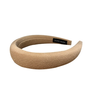 Thick beige padded headband with diagonal ribbed fabric texture and handmade label